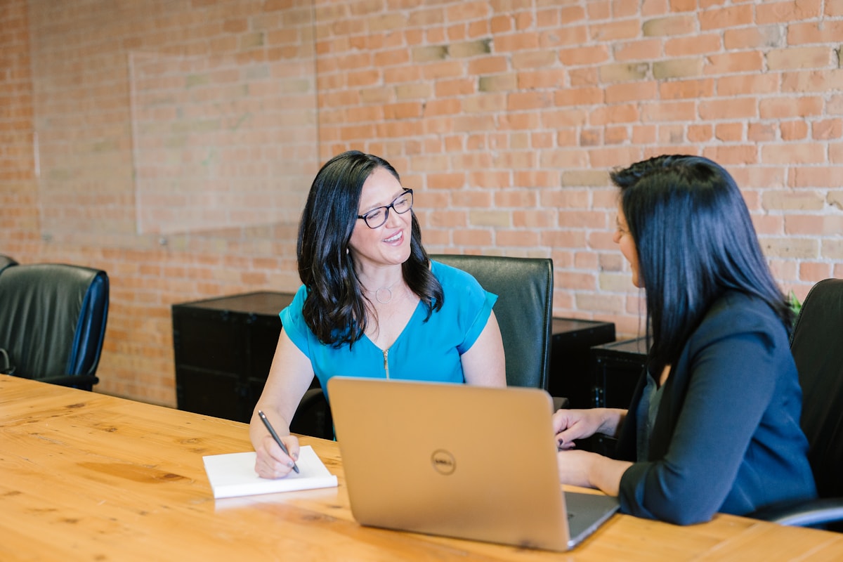 Two professionals talking across a table with a laptop; an illustrative workplace photograph from the RemoRoute image library.